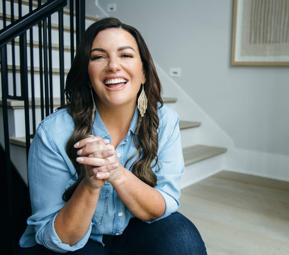 amy porterfield wearing a blue shirt sitting in front of her stairs