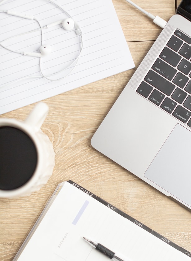 desktop with earbuds, laptop, coffee, and notebook