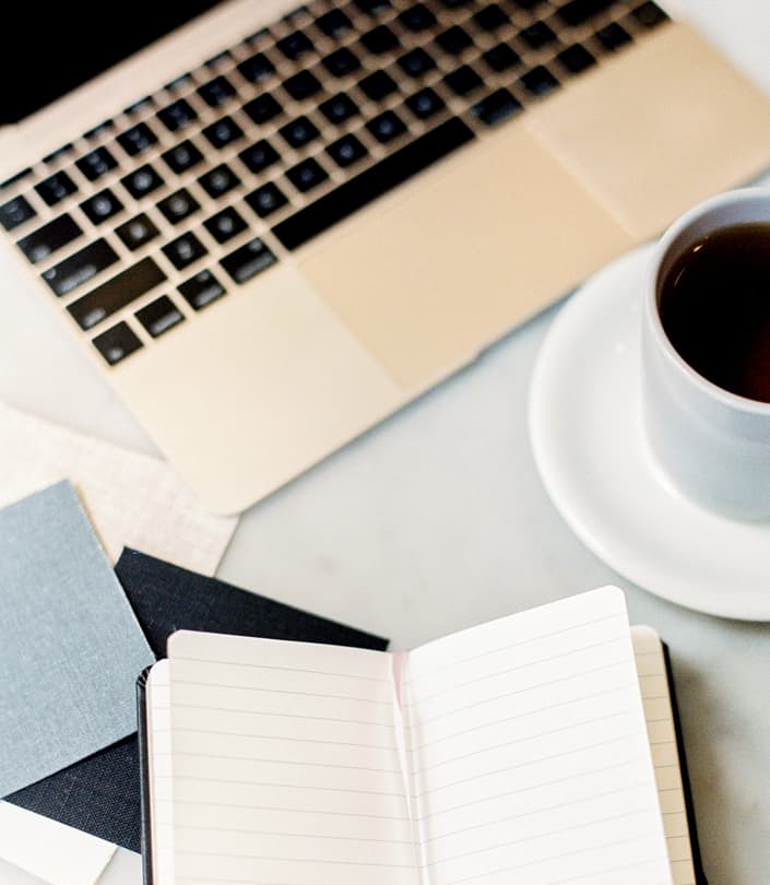 notebook, cup of coffee, and laptop on a desk