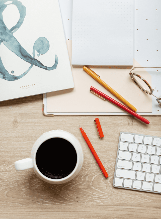 cup of coffee on desk with pens and keyboard